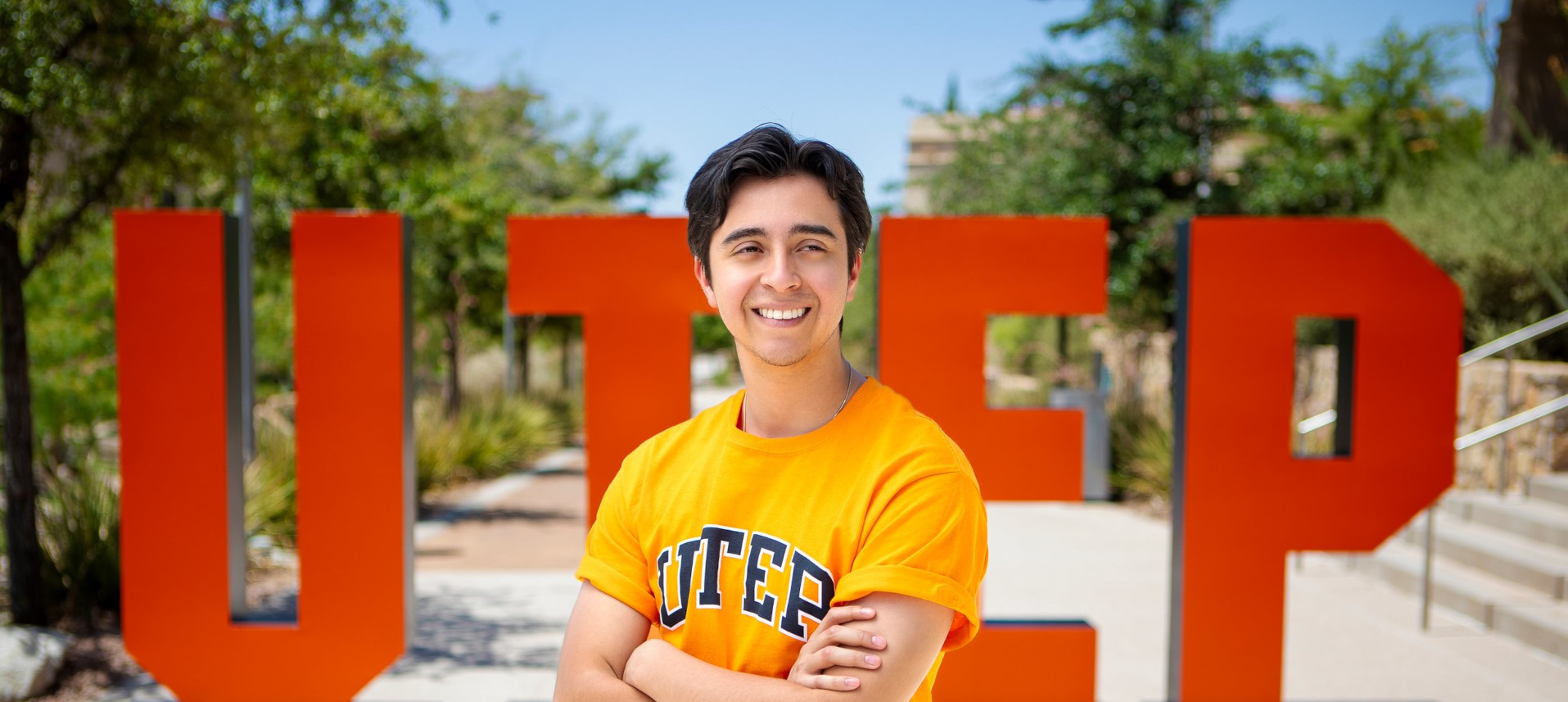 Male student standing with arms crossed in front of the letters, U T E P.